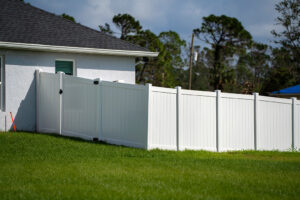 White vinyl picket fence on green lawn surrounding property grounds for backyard protection and privacy.